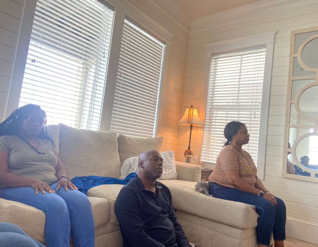 people sitting on couch meditating and deep breathing with eyes closed
