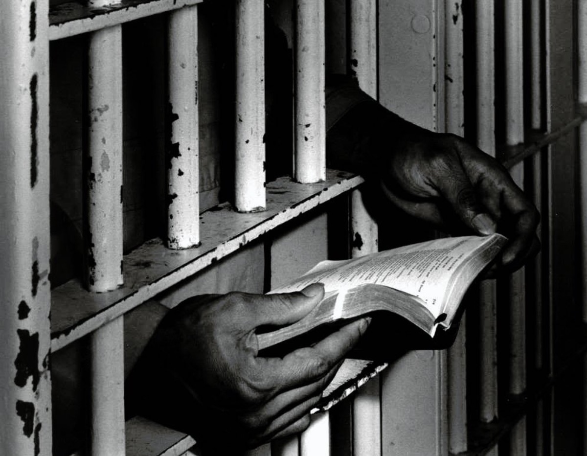 Hands holding bible behind bars