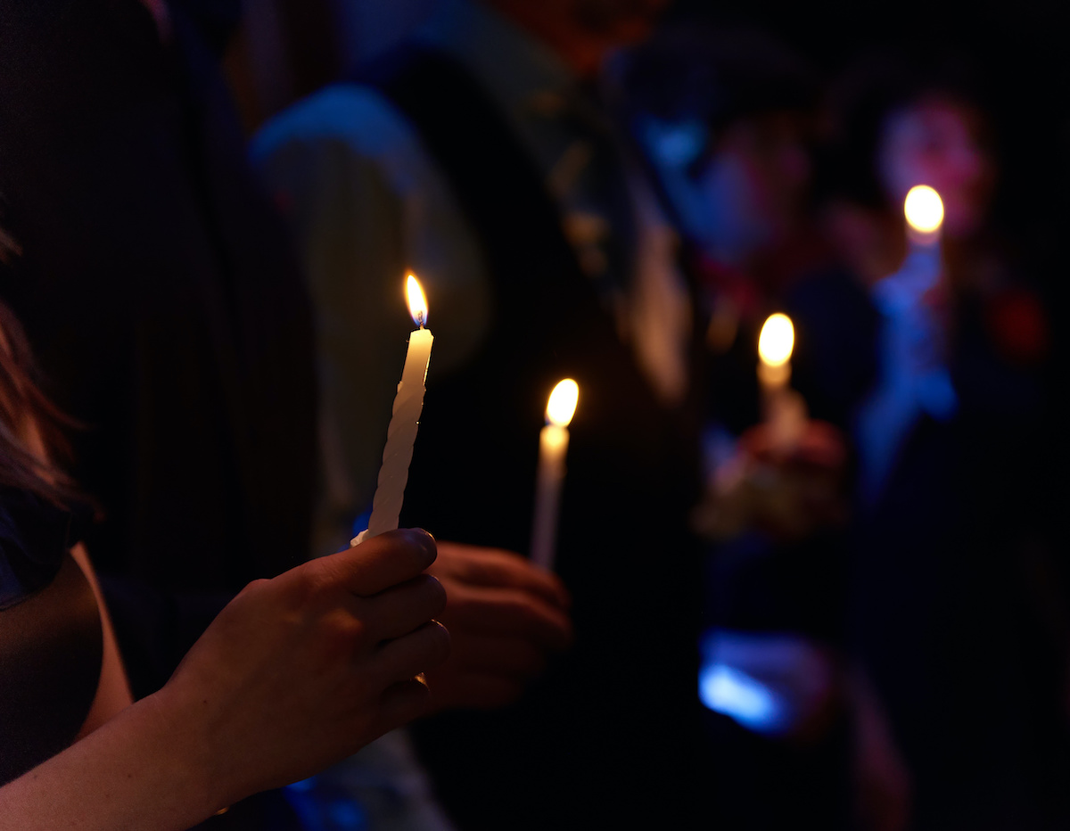 Candlelight vigil. People hold candles light at dark scene