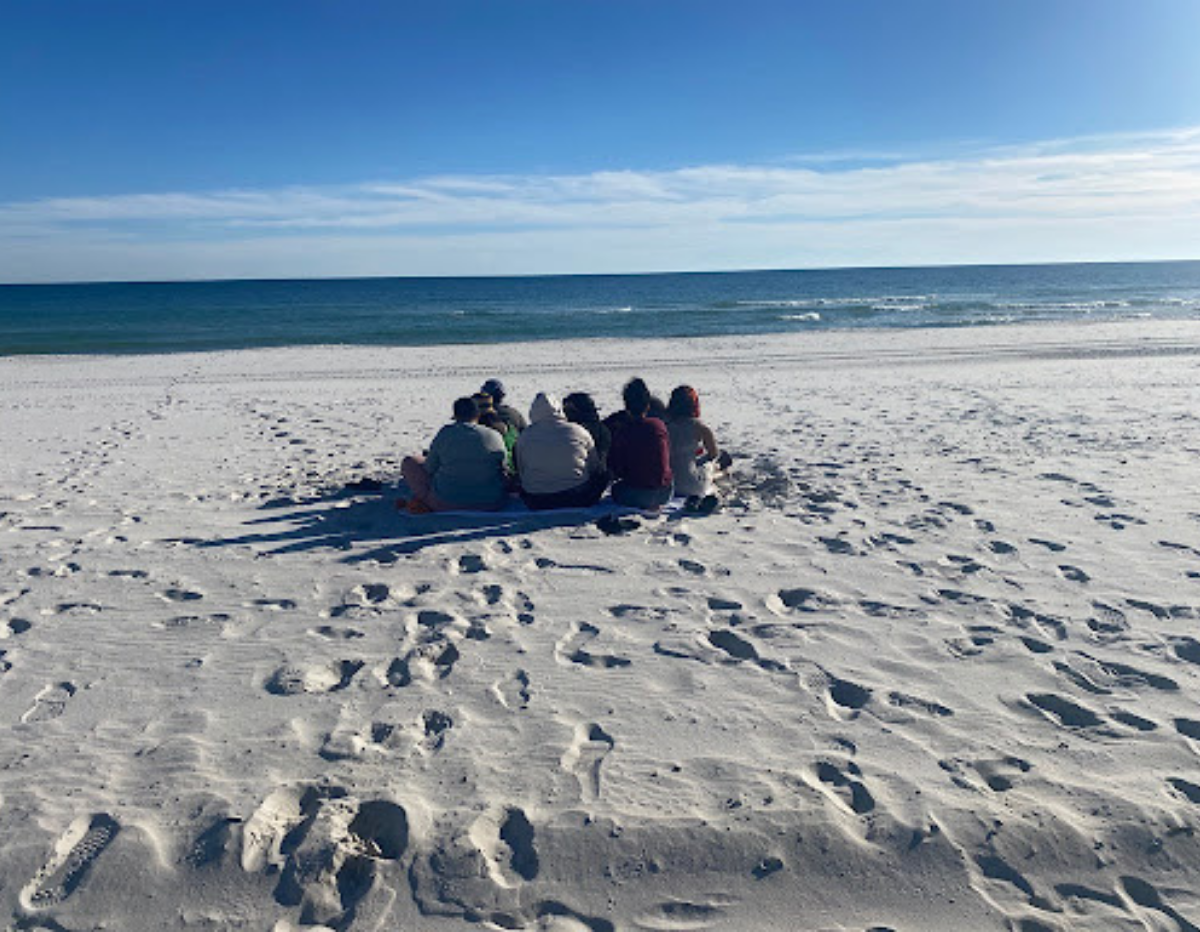 Photo of beach with EJUSA staff on white sand with blue skies