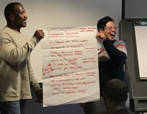 EJUSA Trauma Network member and staff member stand on either side of a poster board that they are using to make a presentation, laughing.