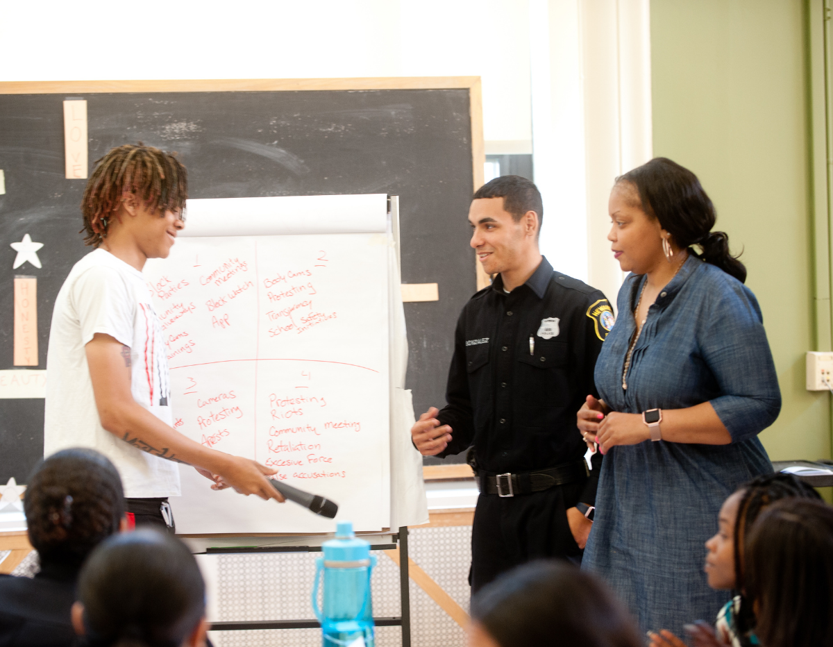 teenage boy and woman talking with police officer at a whiteboard