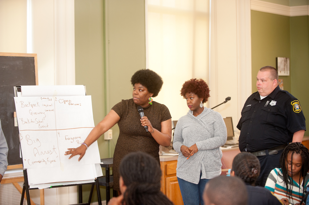 two women pointing to white board next to police officer